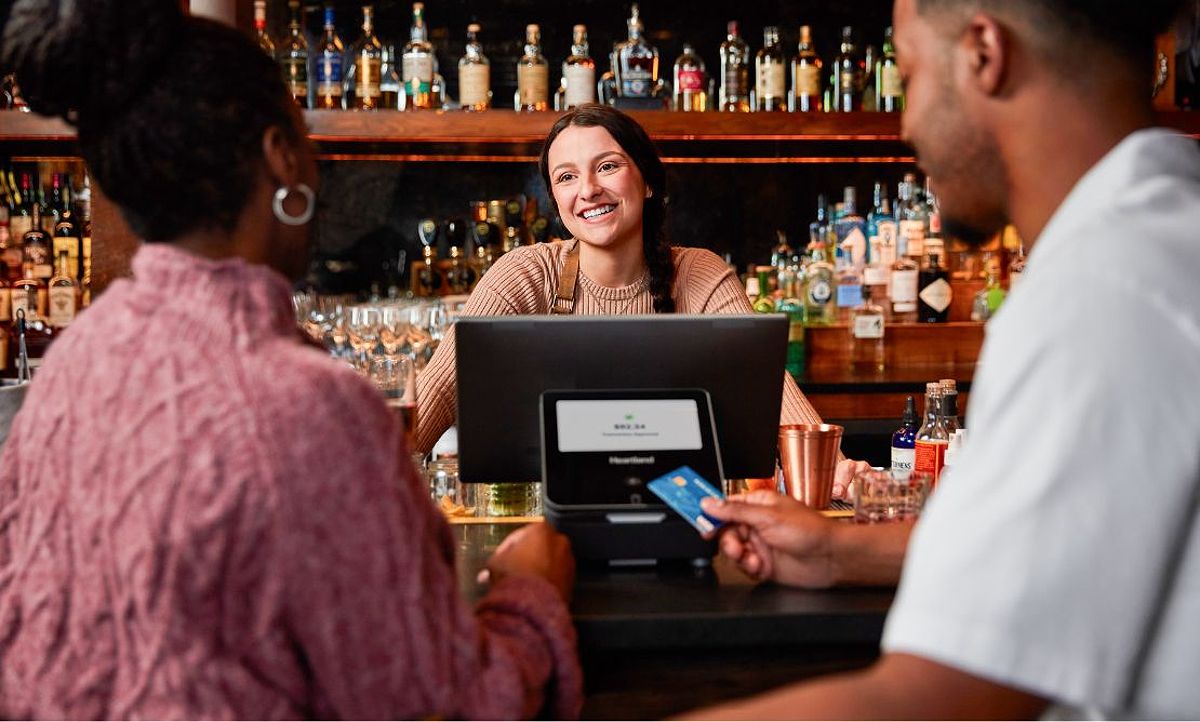 A bartender taking a credit card payment from a couple standing in front of a POS system.