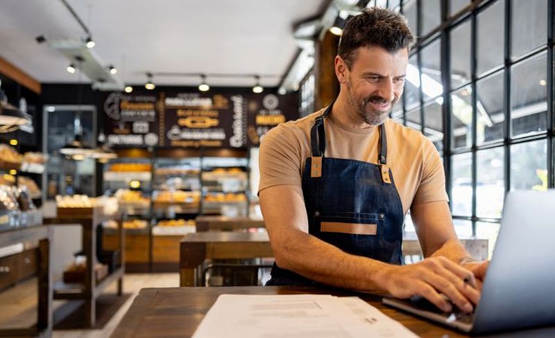 A man in a restaurant smiling and typing on his laptop.