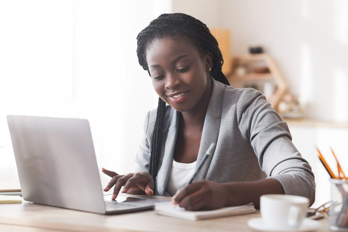 A smiling woman takes notes while using her laptop