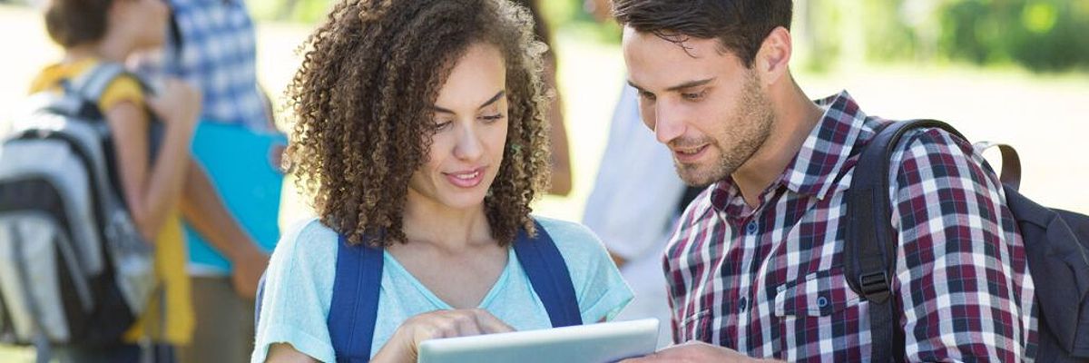 A young woman and a young man look at an iPad together, discussing how to transfer online college credit.